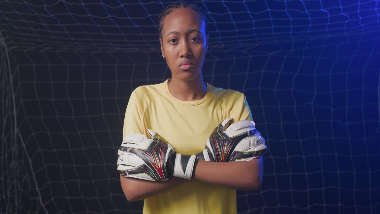 Afrikansk kvinnelig keeper står ved målet og krysser hanskene mens kameraet zoomer inn, viser gul drakt