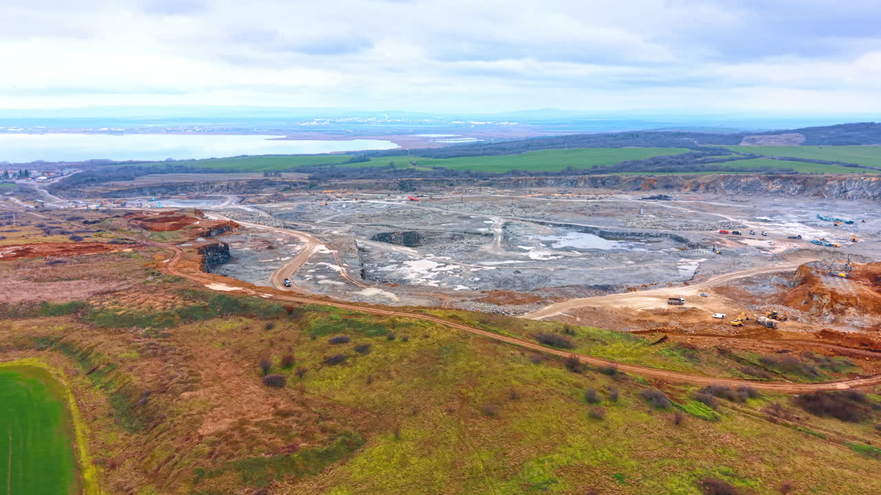 Edilizia rurale a ridosso dell'acqua. Operai stanno spostando materiali in un cantiere accanto all'acqua in un paesaggio rurale sotto cieli nuvolosi.