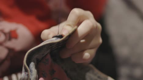 cosiendo un pequeño botón apretado en los jeans desteñidos