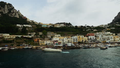 Slowly-drifting-away-from-Capri,-Italy-on-a-boat-while-the-beautiful-view-of-the-harbor,-boats,-and-old-buildings-pass-by