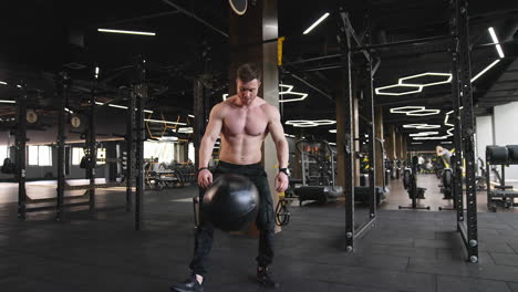 muscular sportsman training in gym. athletic guy lifting and throwing down heavy weights ball in modern fitness center.