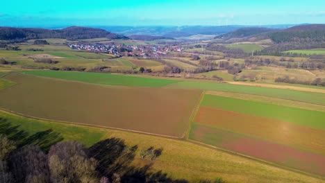 Riesige-Luftige-Weite-Von-Ackerland-Mit-Entfernten-Dorf-Und-Windmühlen