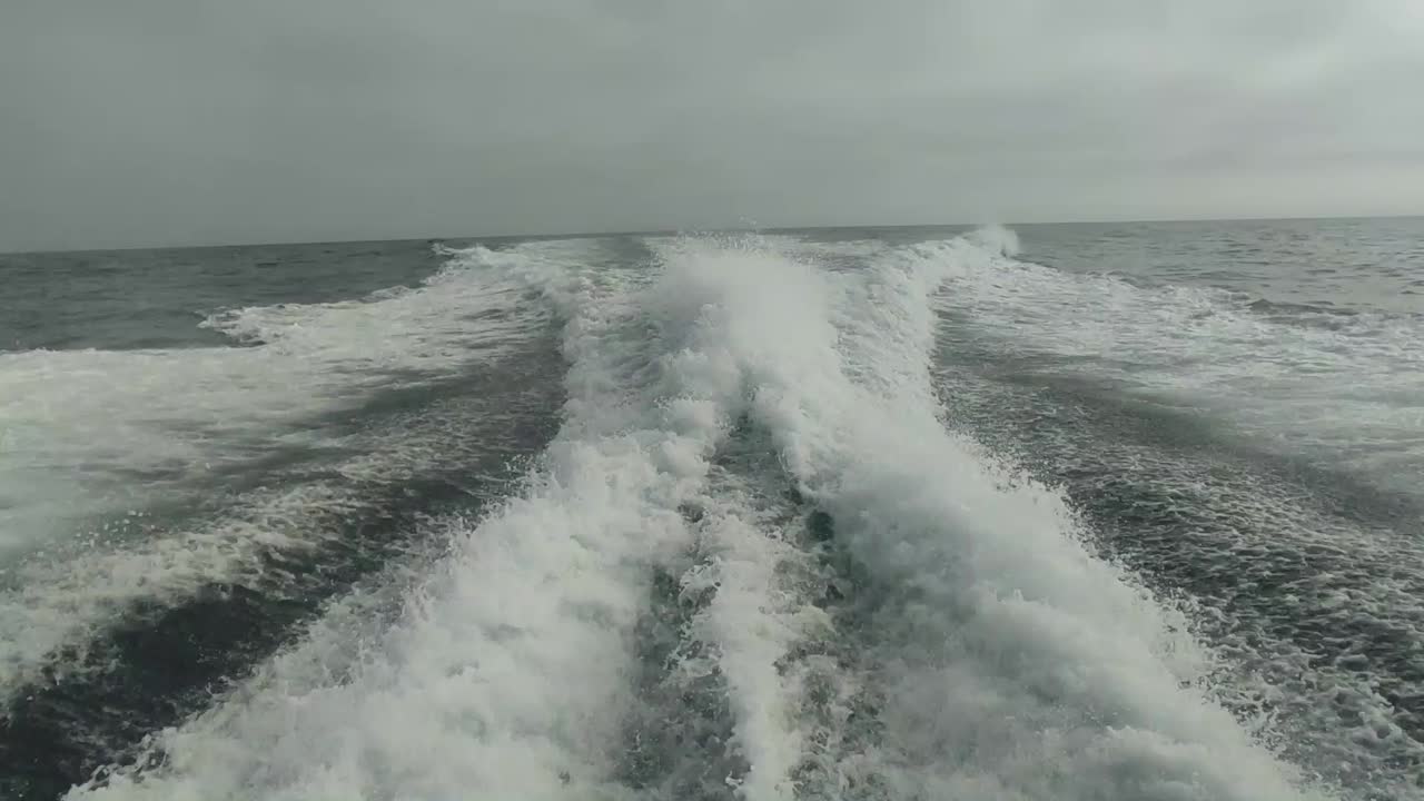 estela de agua vista desde atrás de un bote de motor en movimiento rápido en un día de cielo despejado, mar azul, superficie de agua