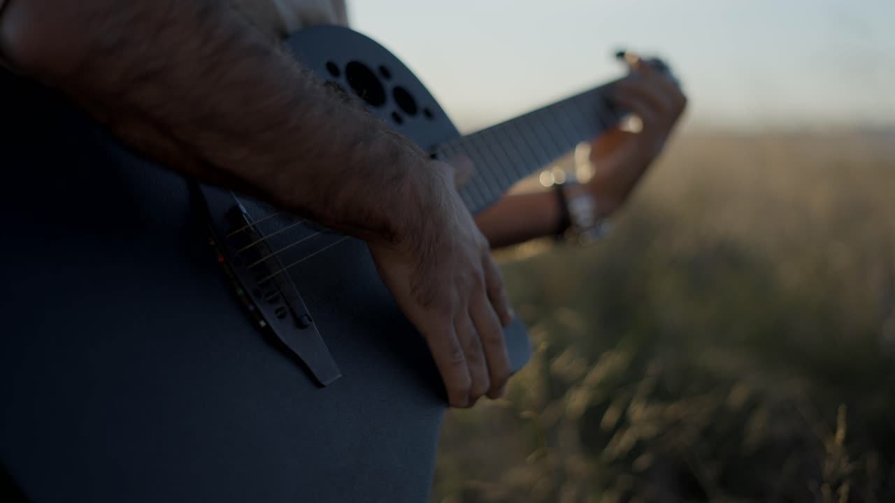 Mann spielt Gitarre auf einem Feld bei Sonnenuntergang