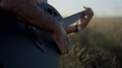 man playing guitar in a field at sunset
