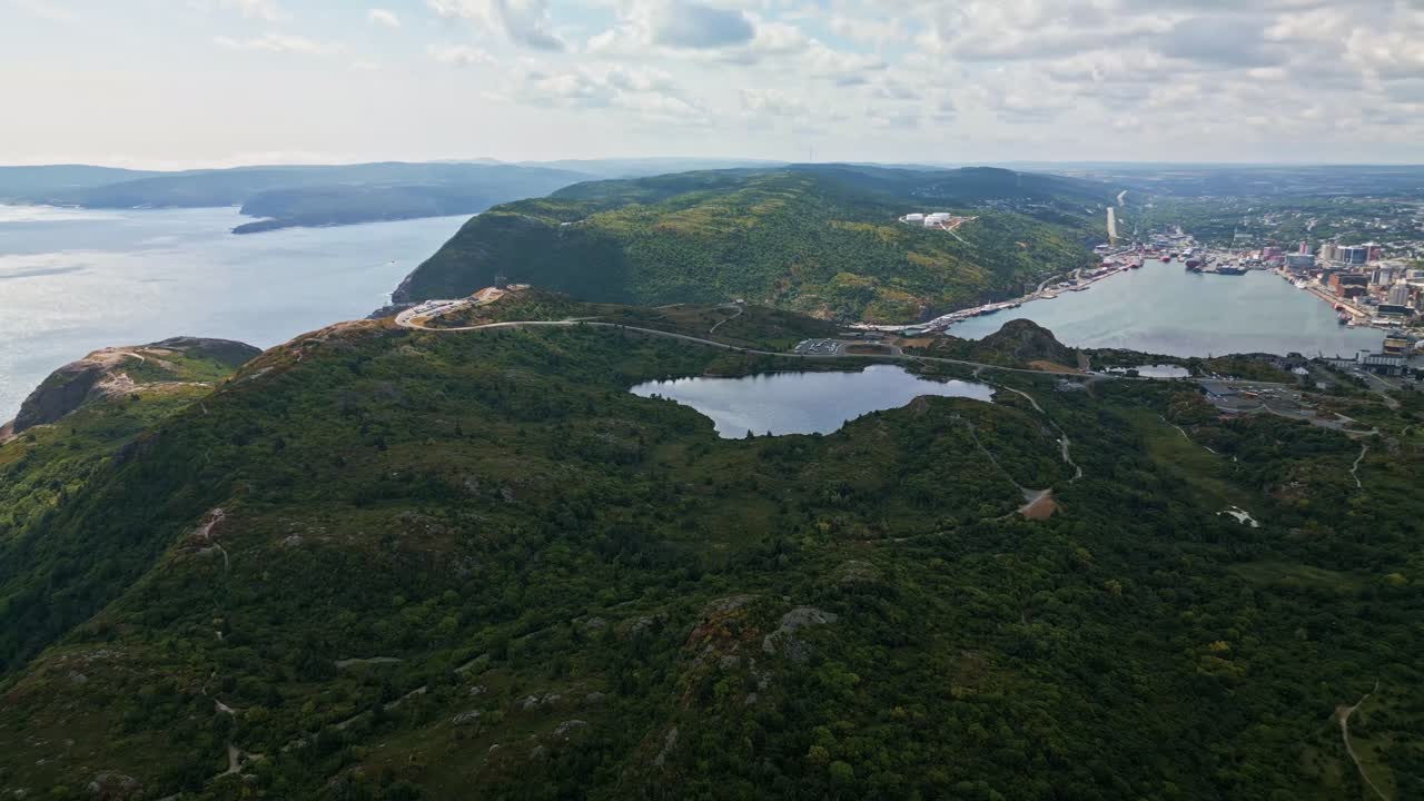 An aerial panorama captures Signal Hill’s rugged cliffs and lush greenery, with historic Cabot Tower on the headland and St. John’s harbour and city skyline stretching below