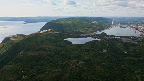 an aerial panorama captures signal hill’s rugged cliffs and lush greenery, with historic cabot tower on the headland and st. john’s harbour and city skyline stretching below