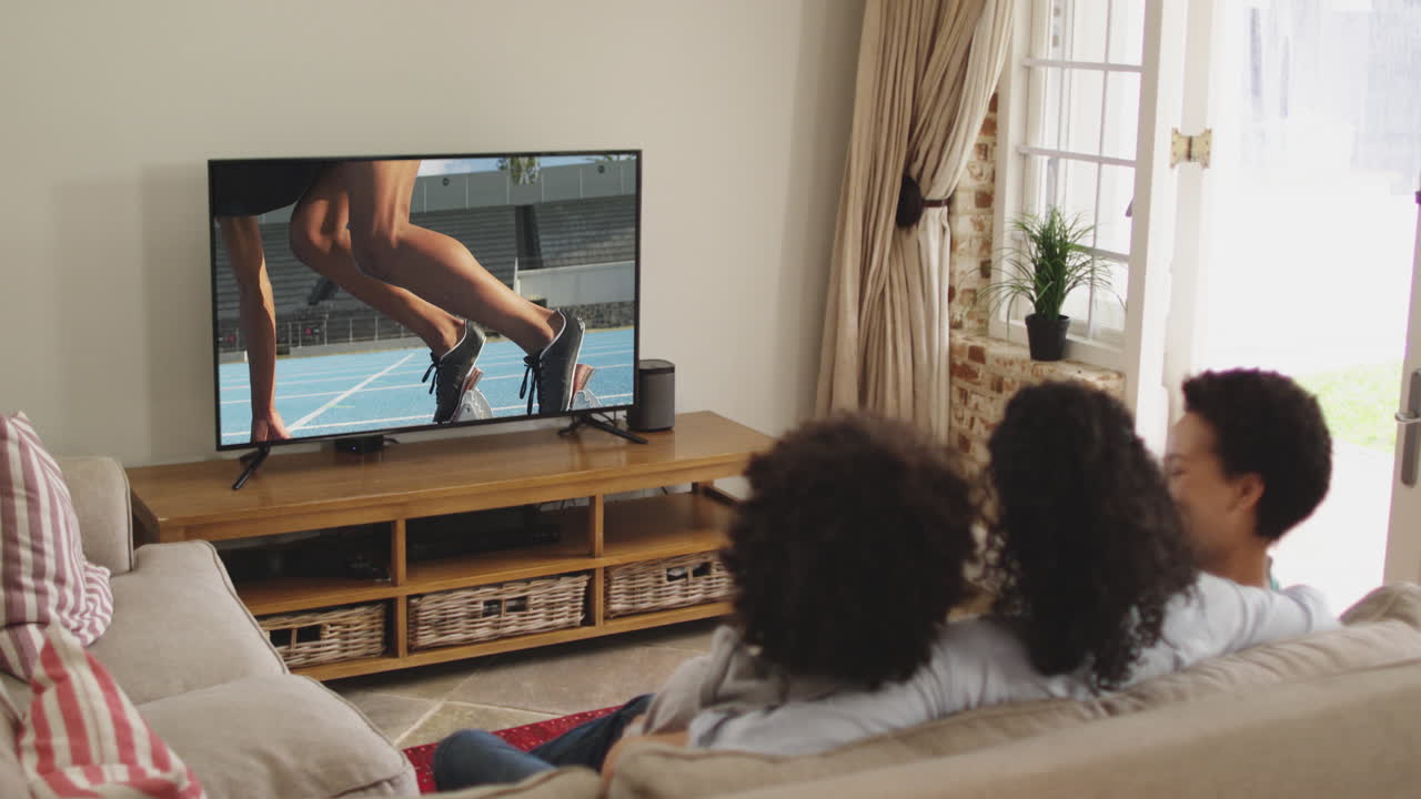 Composizione di famiglia felice seduta insieme a casa che guarda un evento di atletica leggera di corsa in TV.
