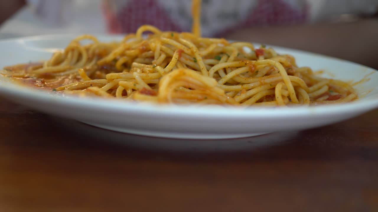 A little girl eats tomato seafood spaghetti in a restaurant. Truck shot from right to left.