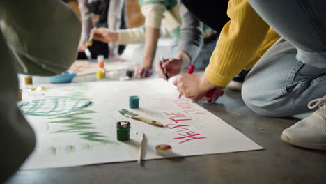 close up of unrecognizable environmental activists painting placards sitting on the floor