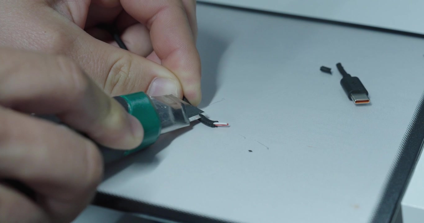 Close-up of hands removing cable insulation with a utility knife during electrical repair work.