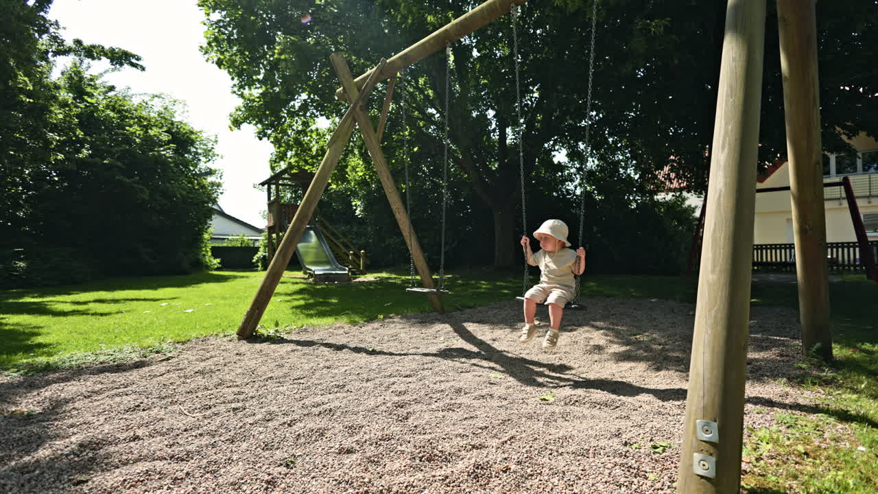 Un bambino con un cappello panama e pantaloncini si dondola su un'altalena in una calda giornata estiva. Un bambino piccolo si dondola in un parco giochi.