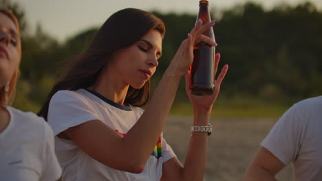 a young girl celebrates a birthday with the best friends. this is carefree open air party with beer on the beach near the lake coast at sunset. she dances and enjoys the time.