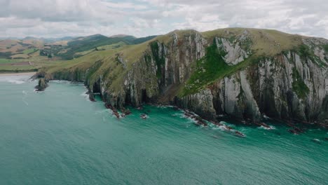 aerial landscape view of steep, rocky and rugged cliff coastline with turquoise ocean in cannibal bay in the catlins, south island of new zealand aotearoa