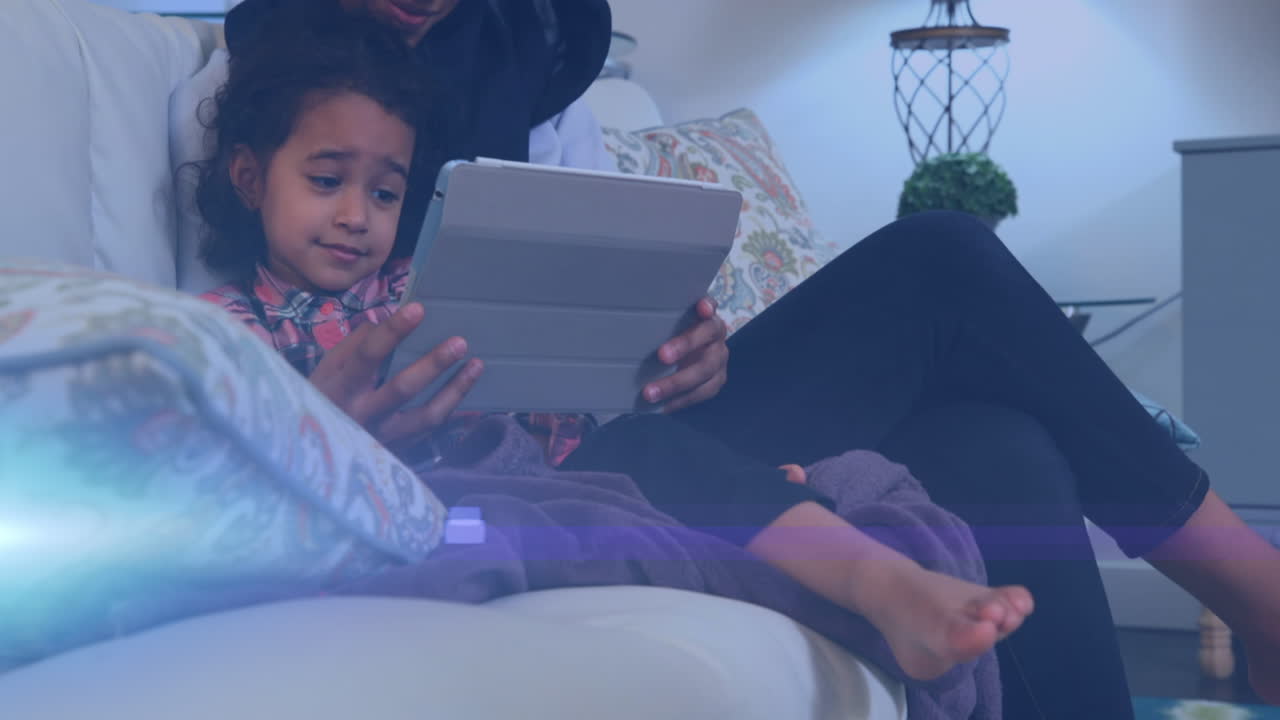 Animation of glowing spots over happy biracial mother in hijab with daughter using tablet
