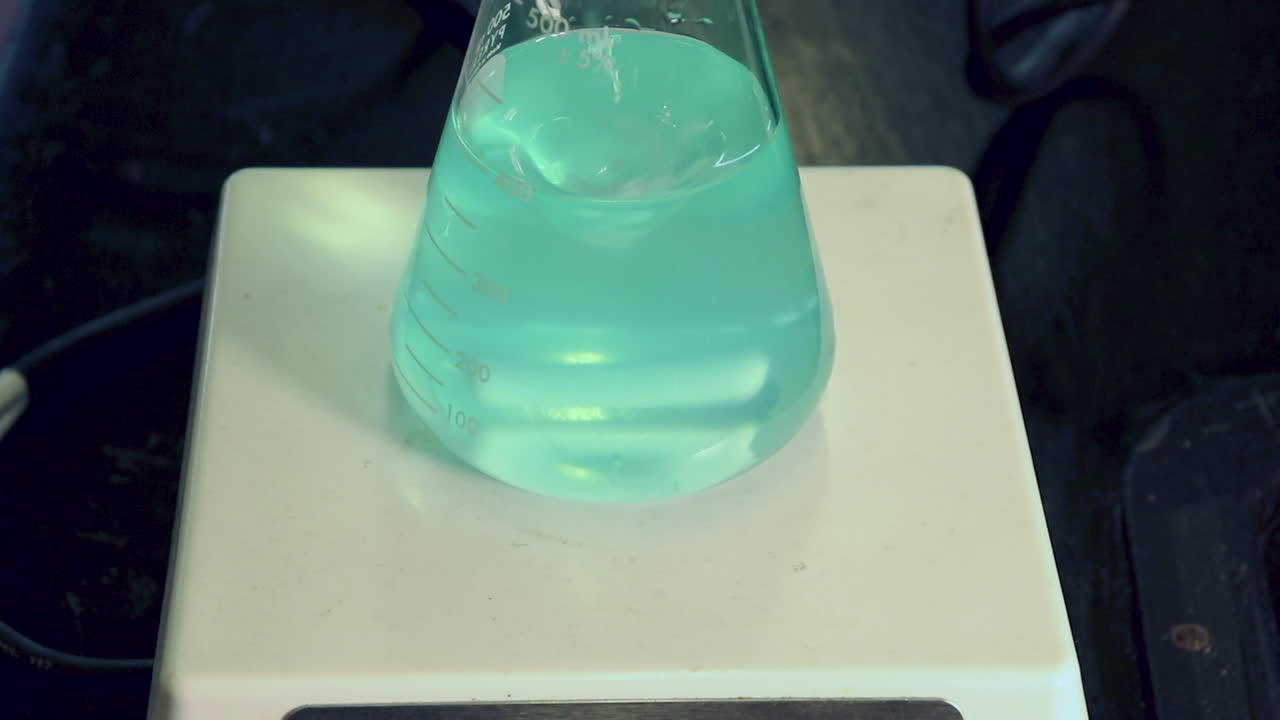 primer plano de una solución azul diluida de sulfato de cobre en un matraz erlenmeyer en un agitador magnético