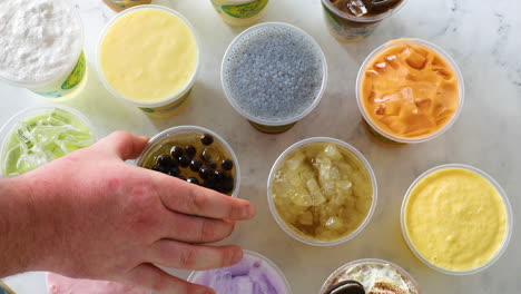 mano masculina recogiendo té helado con boba en la parte superior de un arreglo plano