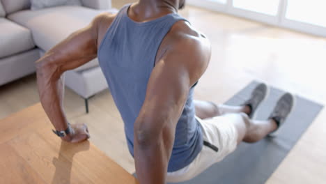 Focused-african-american-man-doing-push-ups-on-table-in-sunny-living-room,-slow-motion