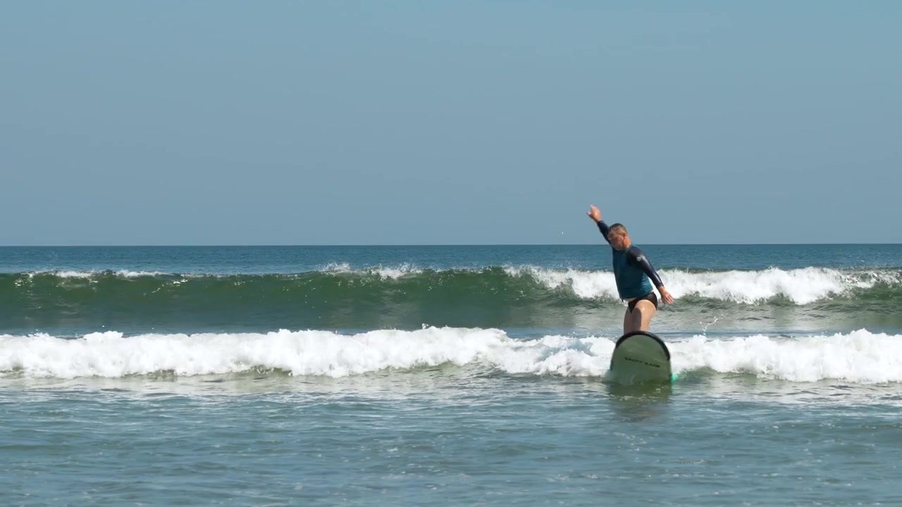 Uomo alla scuola di surf di Kuta Beach, Bali, che cavalca un'onda con un longboard, al rallentatore.