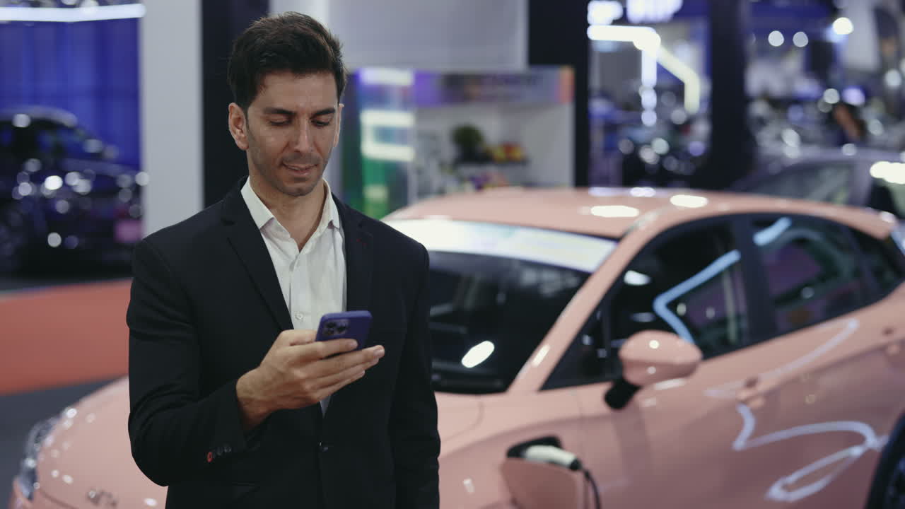 Businessman looking at phone near a pink electric car in a showroom