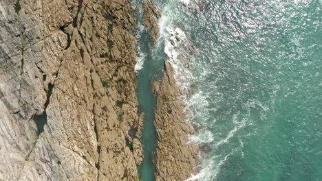 rising aerial shot of waves lapping against a sedimentary cliff on a summer’s day