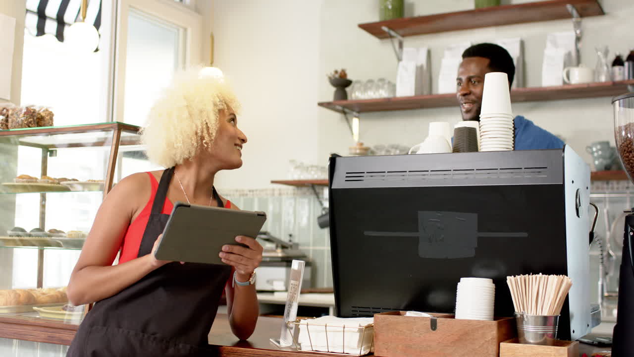 A young African American man and biracial woman use a tablet at a coffee shop