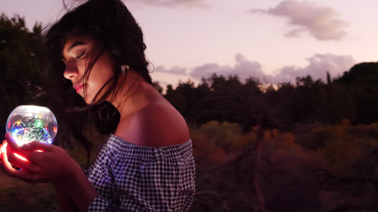 환한 빛으로 빛나는 마법의 영적 구와 함께 환상의 풍경을 헤매는 아름다운 여성 마법사