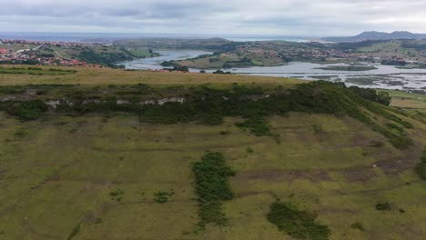 Orbital-flight-over-the-remains-of-a-Paleolithic-settlement-in-a-green-area-and-surrounded-by-a-residential-urban-area-with-mountains-over-the-mouth-of-the-river-to-the-sea-in-Cantabria-Spain