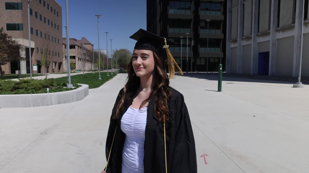 Caucasian female college graduate in cap and gown outside with gimbal camera walking around in slow motion