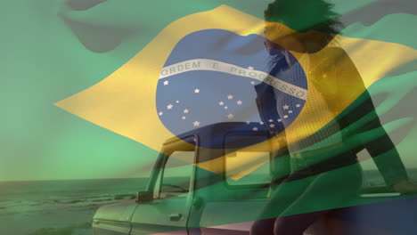 animation of brazilian flag waving over african american woman sitting on pick-up truck at beach