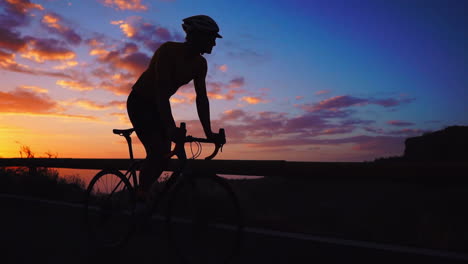 Die-Silhouetten-Zeitlupe-Fängt-Den-Sportler-Ein,-Der-Mit-Dem-Fahrrad-Eine-Serpentine-In-Den-Bergen-Bewältigt-Und-Dabei-Die-Aussicht-Auf-Die-Insel-Genießt.-Dies-Stellt-Ein-Bekenntnis-Zu-Einem-Gesunden-Lebensstil-Bei-Sonnenuntergang-Dar