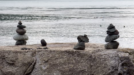 Un-Grupo-De-Mojones-Apilados-En-Una-Gran-Roca-Con-Una-Tranquila-Bahía-De-Agua-Salada-En-El-Fondo