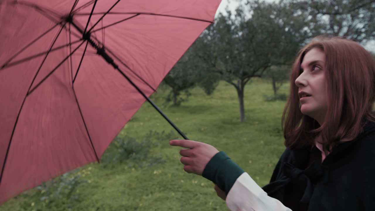 Femme ouvre un parapluie rouge contre la pluie dans un pré en forêt