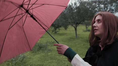 caucasian woman opens red umbrella for rain on a meadow in forest