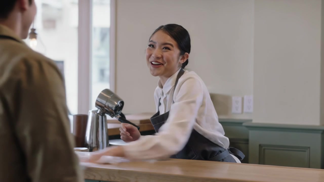 Wiping barista apron cleaning counter with cloth at local cafe smiling speaking, customer entering
