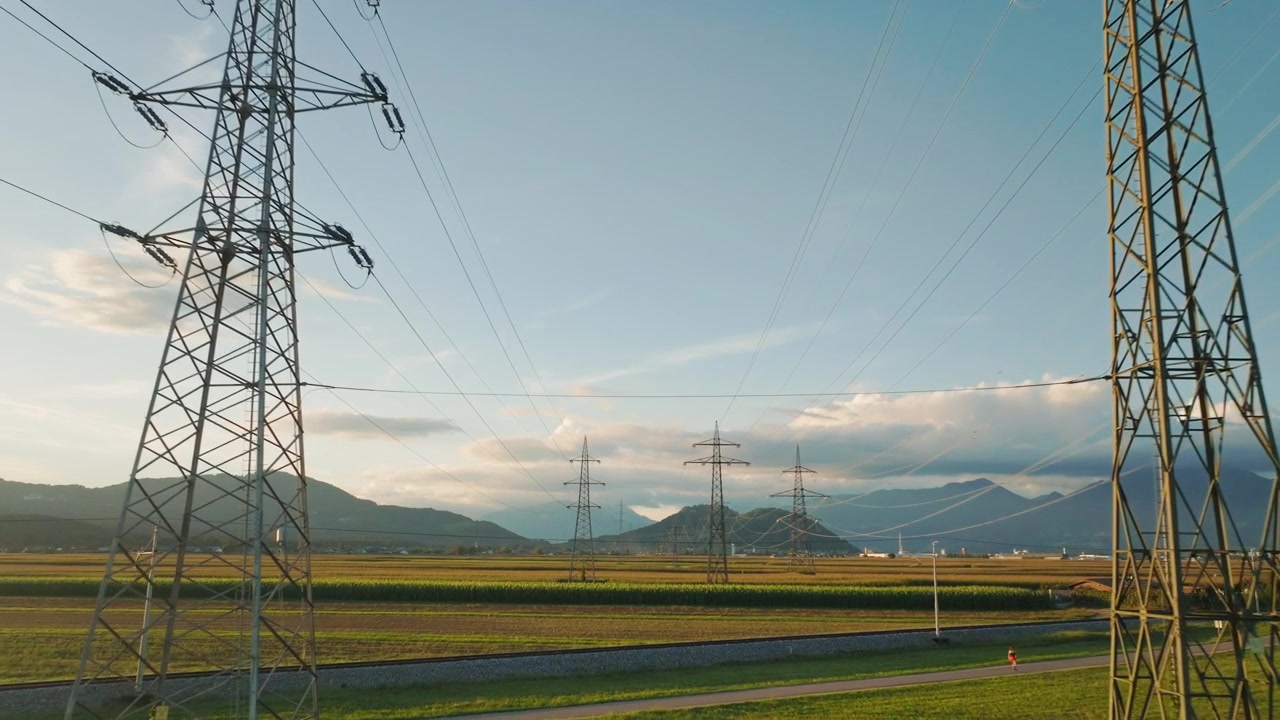 Power lines and towers are visible in a rural area as the sun sets in the background highlighting