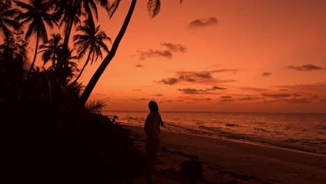 a breathtaking view captures a lone woman strolling along a pristine, palm-lined beach in fuvahmulah, maldives at sunset.