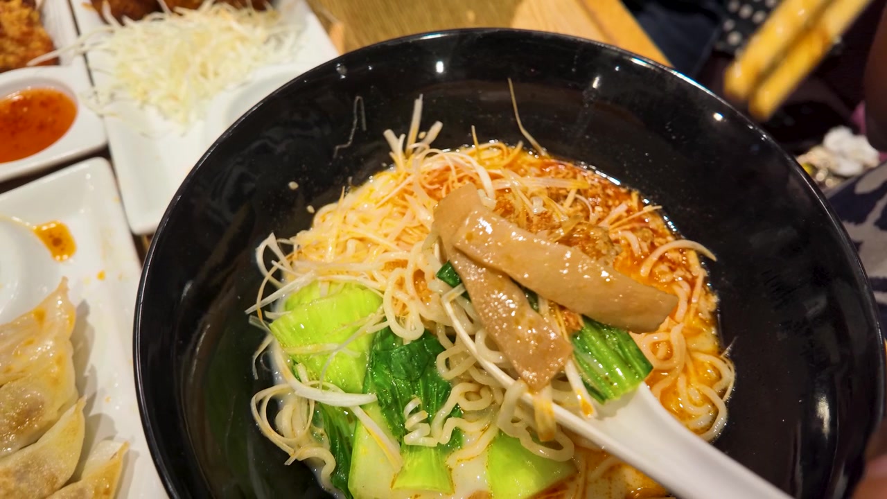 Tampilan Atas Sumpit Mengangkat Mi dari Mangkuk Ramen Pedas dengan Bok Choy dan Gyoza