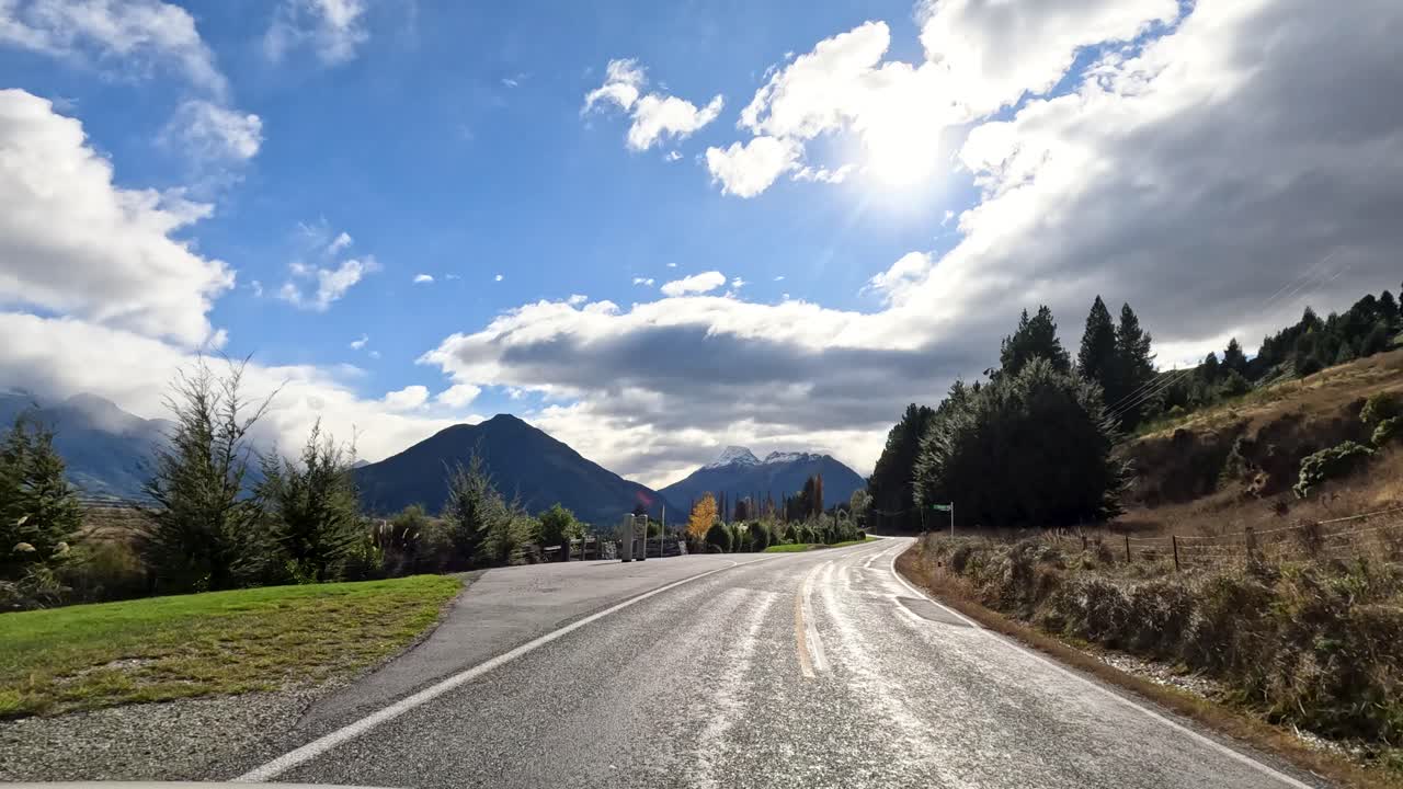 Vehicle travels winding rural road, mountain landscape, partly cloudy sky, natural daylight, forward motion