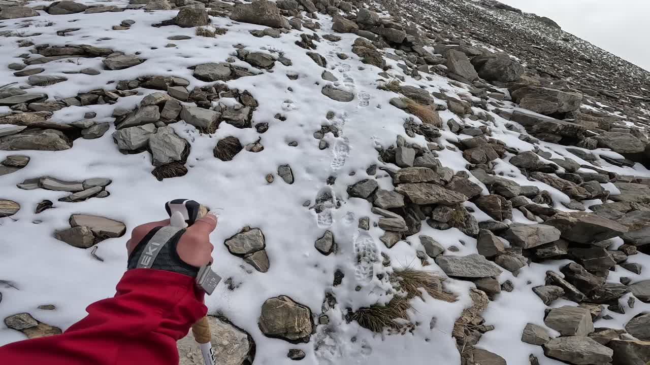 on-board camera, subjective view of a man hiking with poles, on a rocky mountain with snow, then turning to look at the view