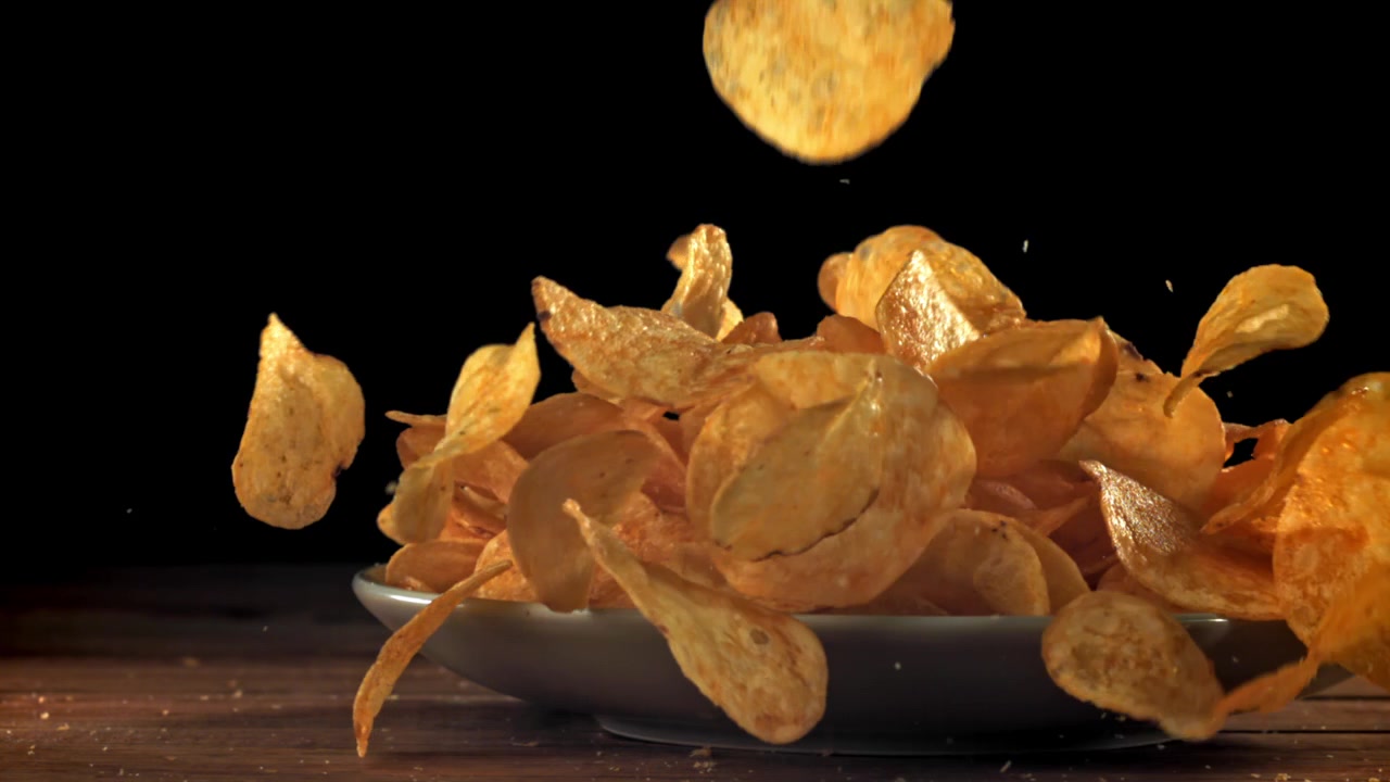 Golden Potato Chips Falling onto a Plate in Slow Motion
