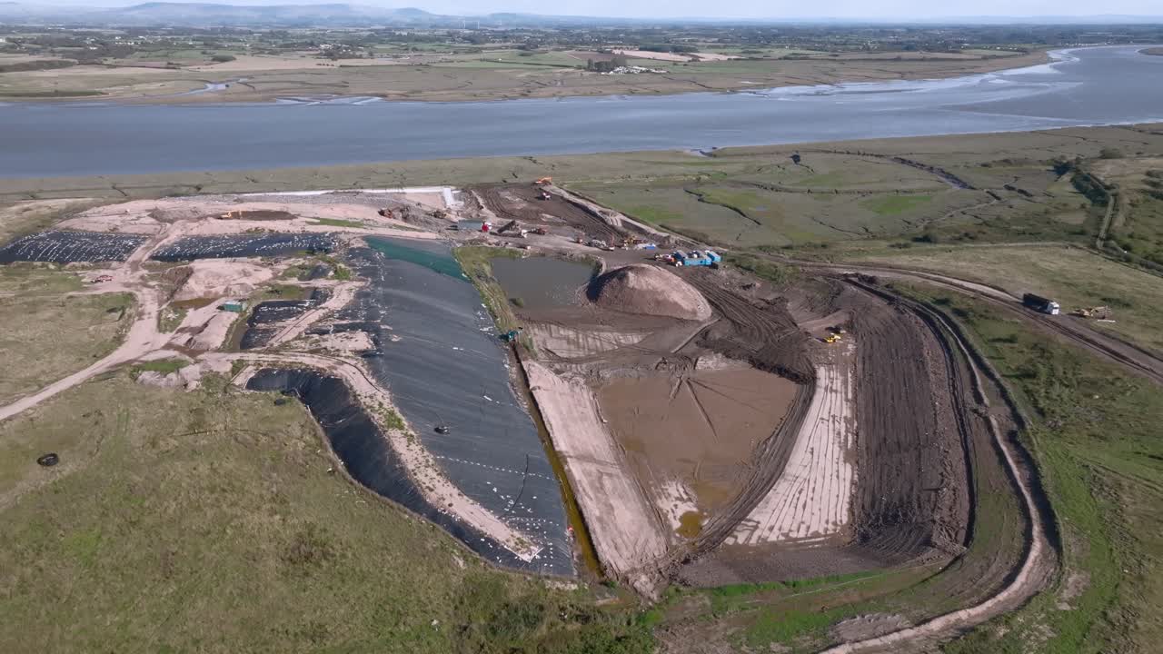 Scarred Landscape Of Landfill Site Next To River Wyre With Moving Vehicles. Jameson Road Landfill And Recycling Site, Fleetwood, UK