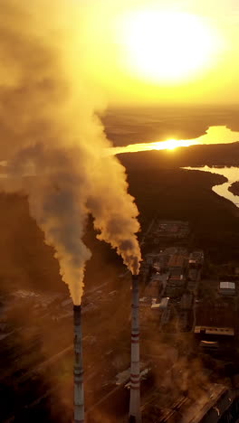 Top view on two pipes with smoke. Factory on the natural fields background at sunset. Pollution the air. Aerial view. Vertical video