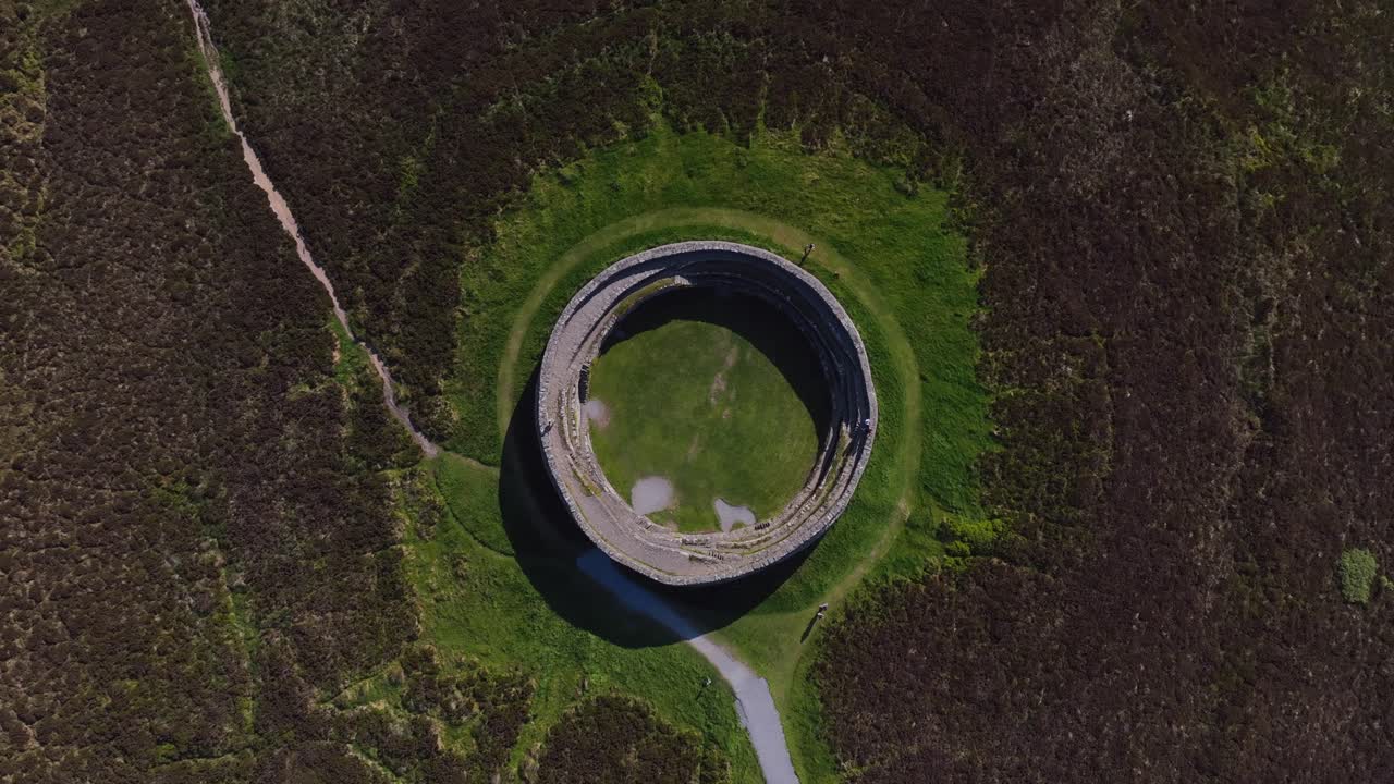 Grianan of Aileach, County Donegal, Ireland, June 2023. Drone Bird's Eye view ascent and clockwise rotation above the iconic Gaelic ringfort at Inishowen surrounded by grassy fields and wild heather.