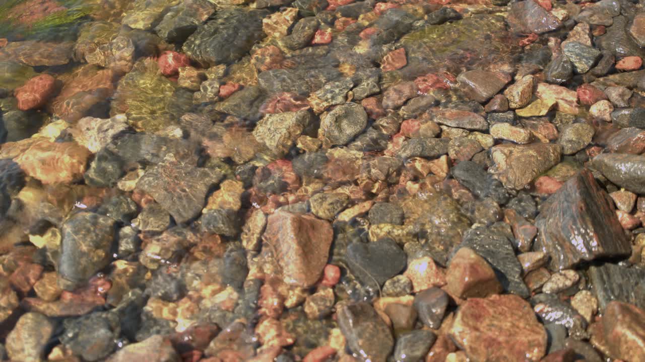 Acqua fredda e limpida lambisce dolcemente le rocce dorate sulla riva ghiaiosa del lago