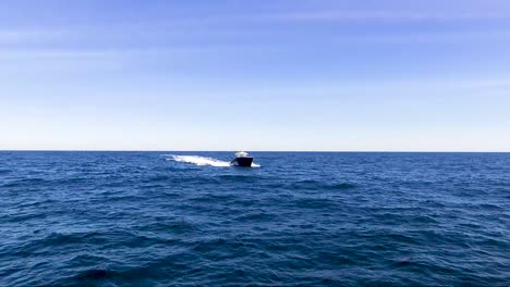 Drone-tracking-a-fast-boat-in-the-open-ocean-on-a-bright,-sunny-day-with-blue-sky-and-blue-water