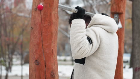 young man leaps onto workout equipment, performs a quick pull-up and drops down, framed by a snowy background with bare trees