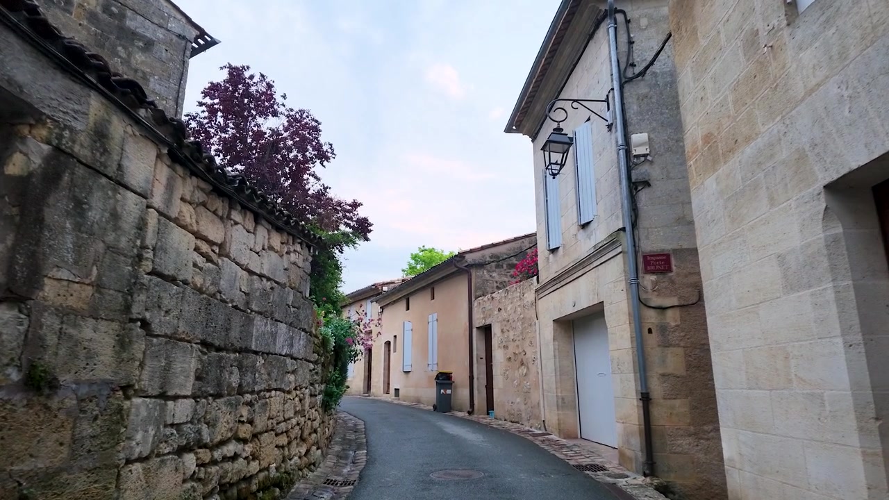 Una ripresa in movimento dal basso attraversa uno stretto vicolo medievale con edifici storici in pietra calcarea.
