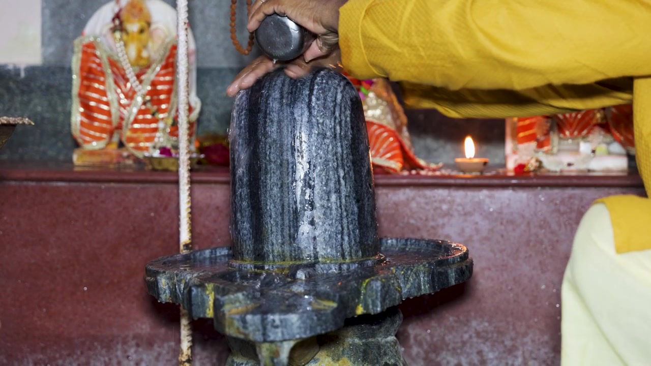 Devoto indù che esegue il rituale Abhishek del Shiva Lingam all'interno di un sacro santuario del tempio.