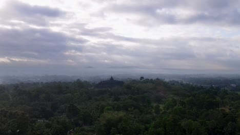 aerial approaching shot of asian countryside and borobudur temple during cloudy day in the morning - establishing drone shot